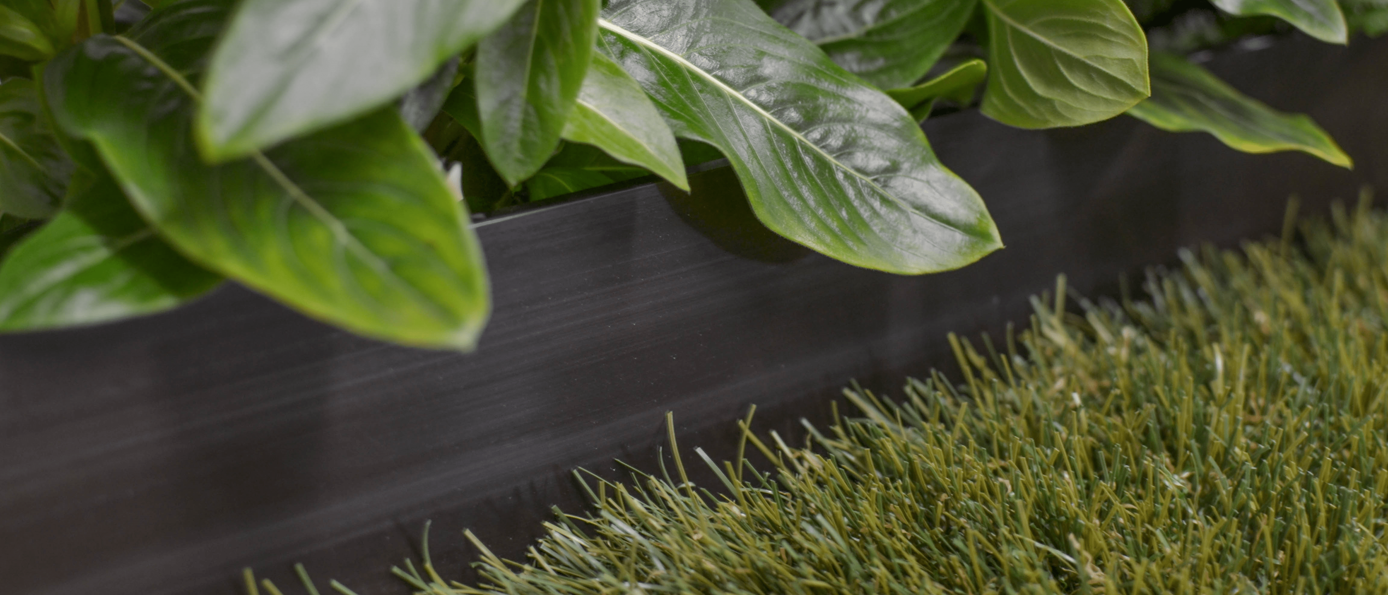 Picture of black aluminum garden edging. Synthetic turf is butted up against it with decorative leaves.